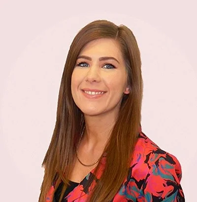 Woman with long brown hair and colourful jacket looking at the camera
